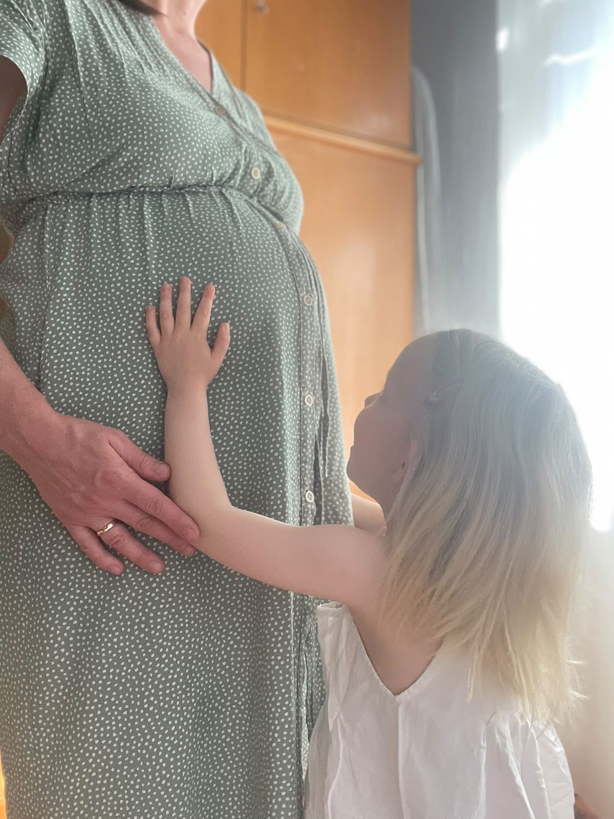 Schwangere Mutter, deren Geschwisterkind die Hand an den Babybauch legt