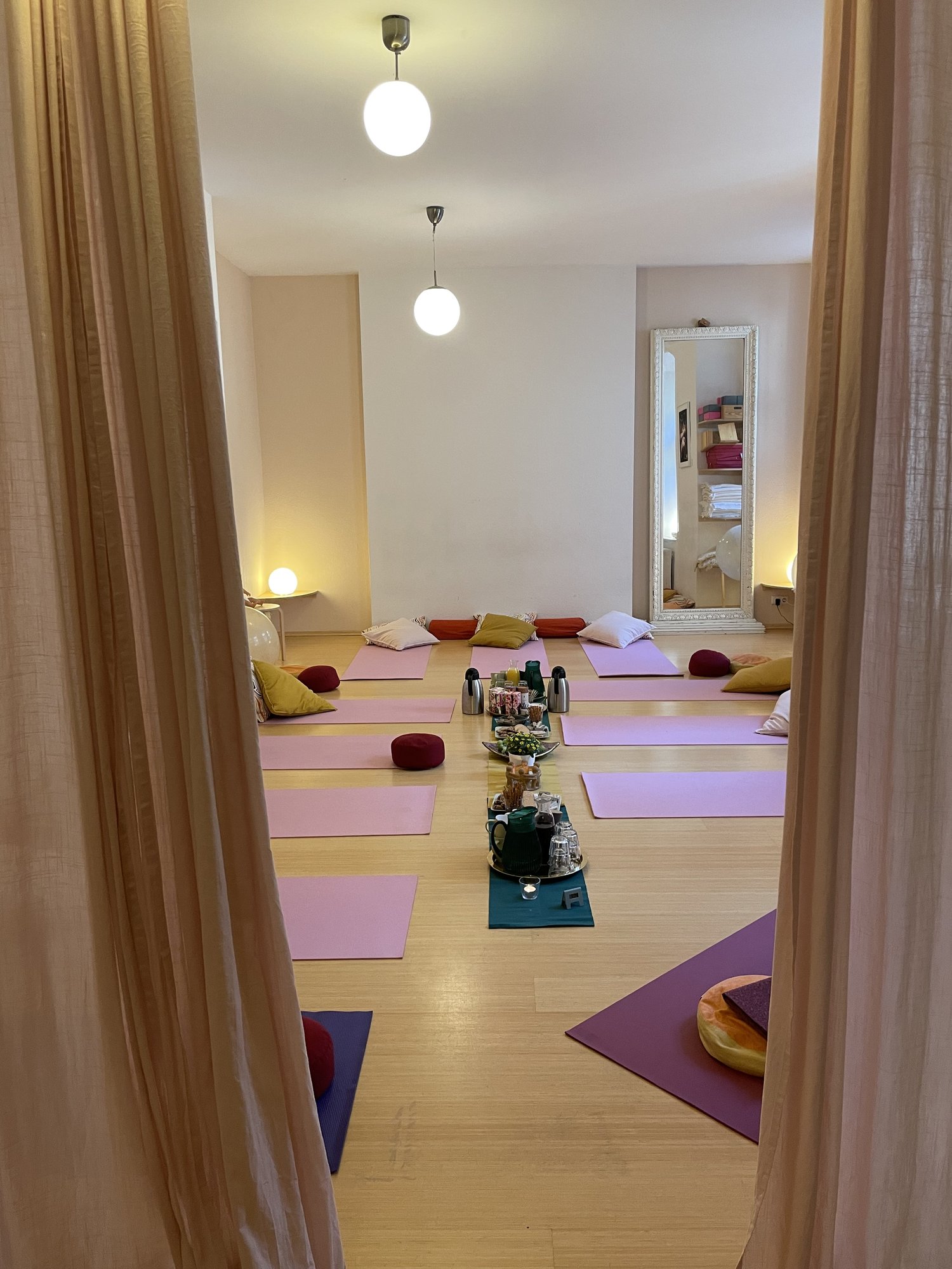 Vorbereiteter Yogaraum mit rosa Matten, durch Vorhang gesehen