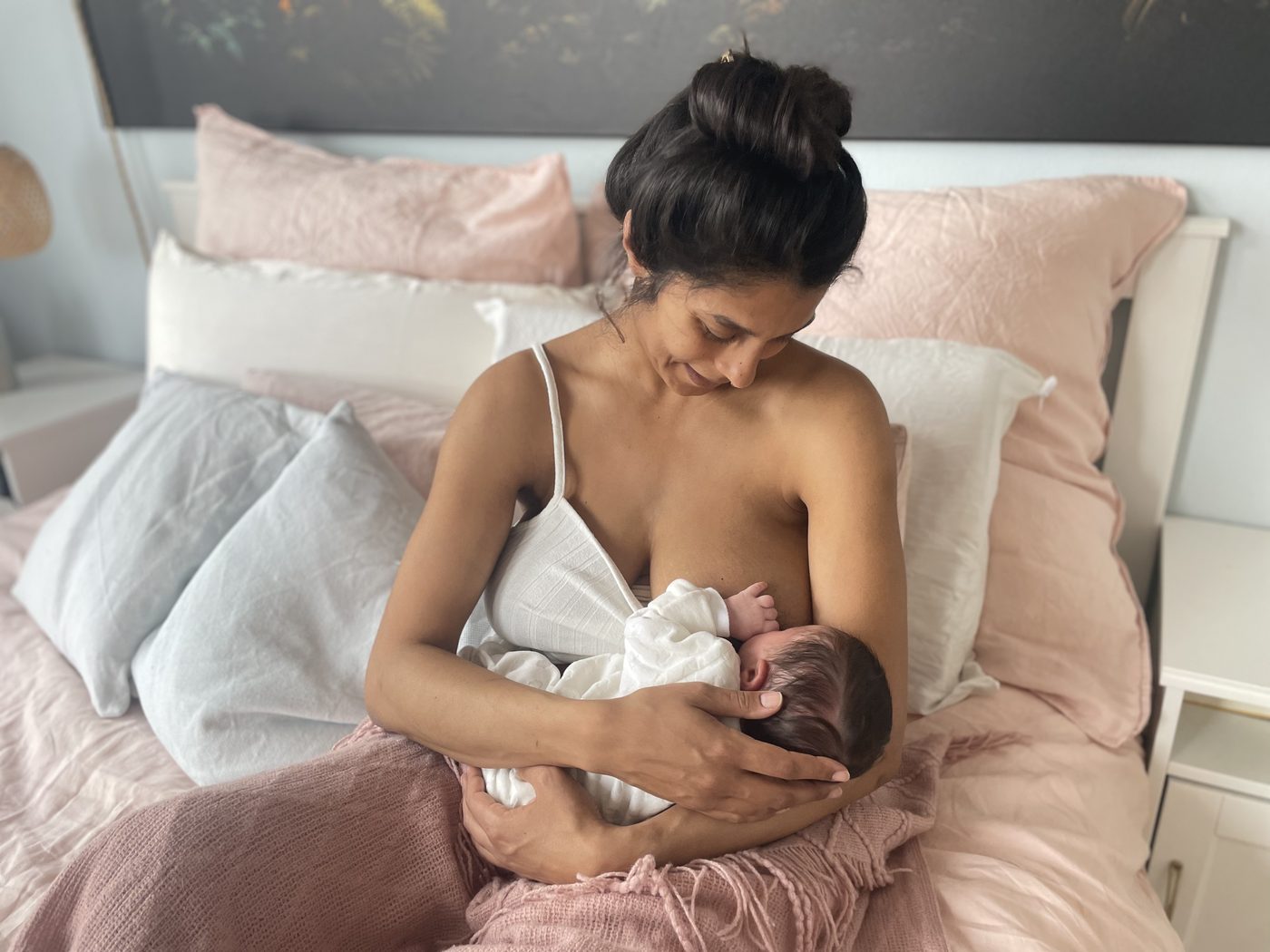 Mutter sitzt entspannt auf dem Bett und stillt ihr Baby